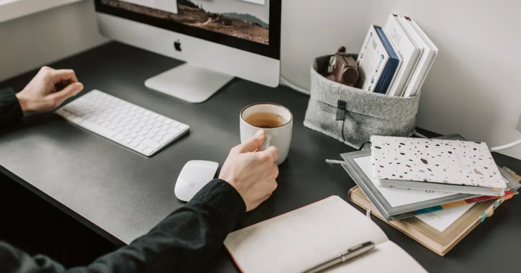 notebook e caderno abertos em cima de uma mesa de trabalho com uma xícara de café